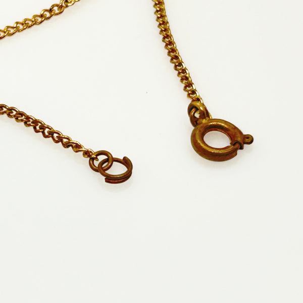 A close-up of a gold-toned chain necklace showing a spring ring clasp  on a plain white background.