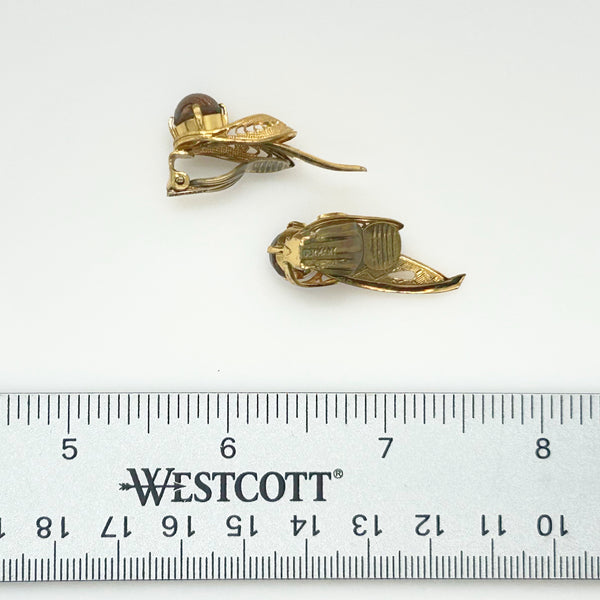 A pair of gold-toned beetle-shaped earrings with a dark brown bead and clear crystal accents, displayed above a Westcott brand ruler on a white background.