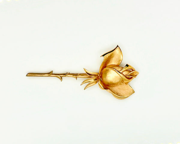 Vintage Crown Trifari gold-tone long-stem rose brooch featuring a detailed, textured matte rosebud on a thorny gold stem against a clean white background.