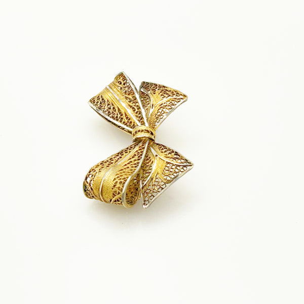 Side angle view of a vintage gold filigree bow brooch showcasing the dimensional openwork ribbon folds on a white background.