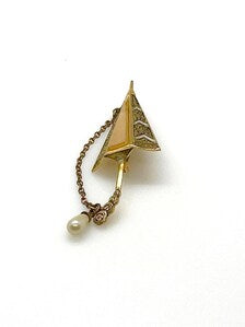 Vintage Spanish Damascene umbrella brooch with gold-tone filigree canopy panels, detailed red and black enamel patterns, a triangular mother of pearl inlay, and a dangling gold chain with a teardrop faux pearl charm against a plain white background
