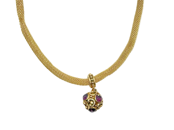 This 1990s pendant necklace features a meticulously crafted design with round purple faceted gemstones set in bezel-mounted antiqued gold metalwork. The ornamental pendant is suspended from a rounded mesh chain, measuring 16" secured with a toggle clasp.