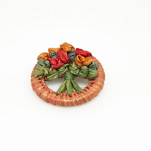 This beautiful antique brooch, likely dating back to the early 1900s, is quite rare. It showcases a charming design with colored straw wrapped around a circular frame. Inside, you'll find a delicate, hand-crafted tree or bouquet made from fine threads.