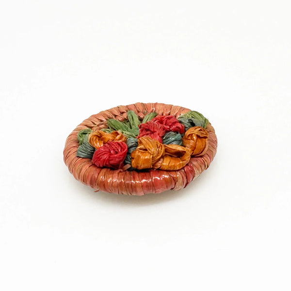 This beautiful antique brooch, likely dating back to the early 1900s, is quite rare. It showcases a charming design with colored straw wrapped around a circular frame. Inside, you'll find a delicate, hand-crafted tree or bouquet made from fine threads.