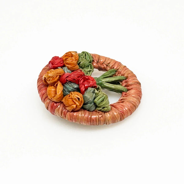 This beautiful antique brooch, likely dating back to the early 1900s, is quite rare. It showcases a charming design with colored straw wrapped around a circular frame. Inside, you'll find a delicate, hand-crafted tree or bouquet made from fine threads.