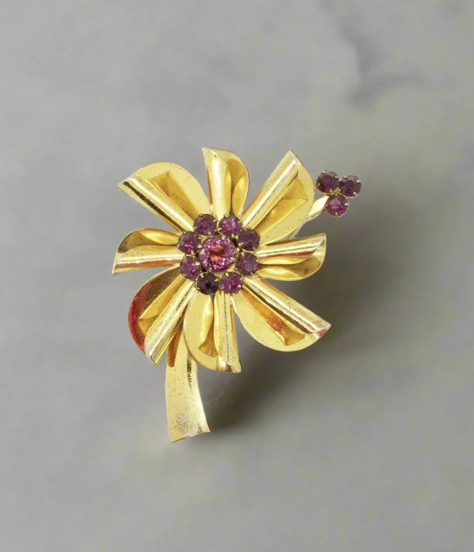 This is a an exemplary example of the floral pins made in sterling with a gold wash from the last century. A purple faceted stone is surrounded by smaller purple stones, and three more accent the top of a petal. 