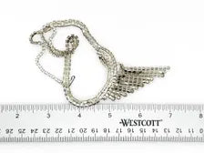 A silver-toned metal chain necklace with a wing-shaped pendant, displayed on a white background above a Westcott brand ruler for scale.