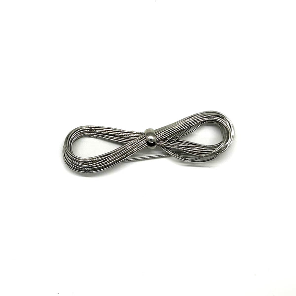 A silver-toned multi-strand wire bow brooch, featuring an infinity-shaped loop silhouette cinched with a smooth central band, displayed against a plain white background.