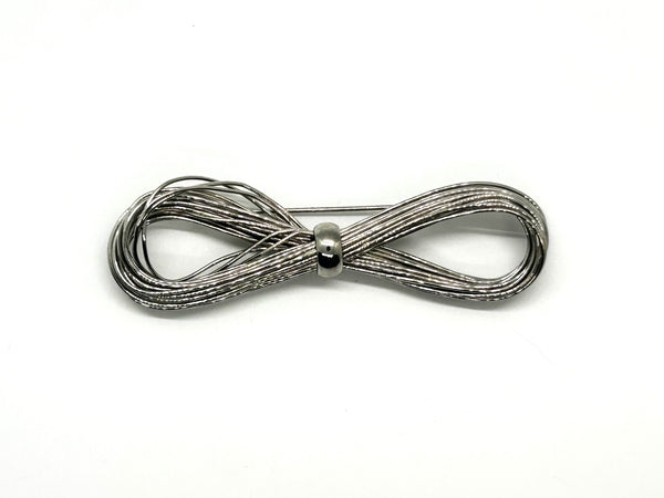 A silver-toned multi-strand wire bow brooch, featuring an infinity-shaped loop silhouette cinched with a smooth central band, displayed against a plain white background.