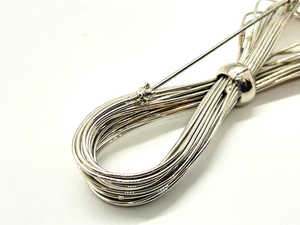 A silver-toned multi-strand wire bow brooch, featuring an infinity-shaped loop silhouette cinched with a smooth central band, displayed against a plain white background.
